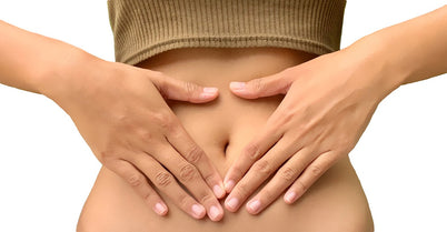  A woman gently holds her stomach with both hands, expressing a moment of contemplation or discomfort.